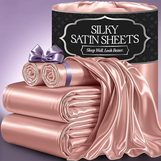 Blush pink satin sheets with smooth, shiny texture, including folded and rolled pieces with a purple ribbon.