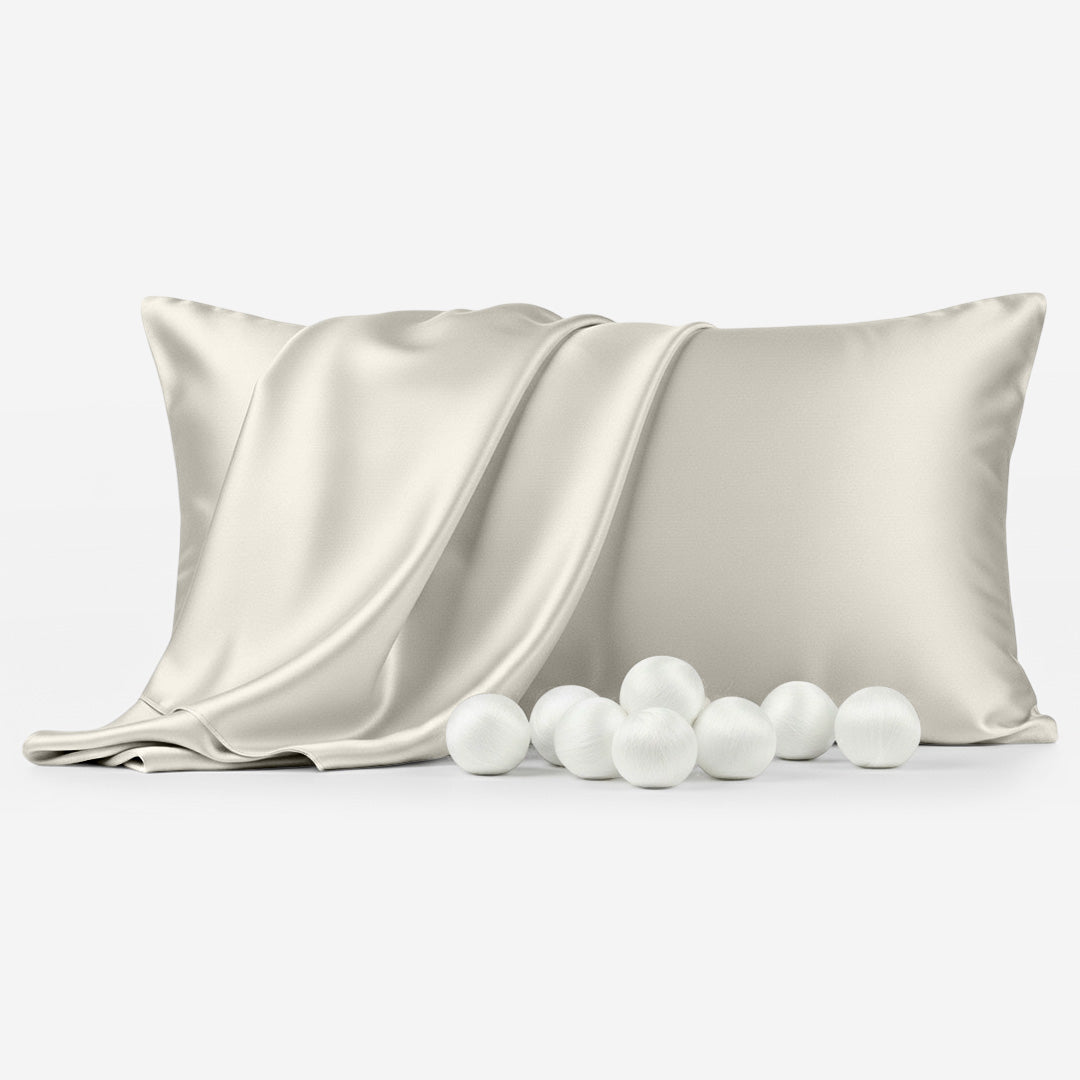 Ivory silk pillowcase with smooth sheen draped over pillow, surrounded by white silk balls.