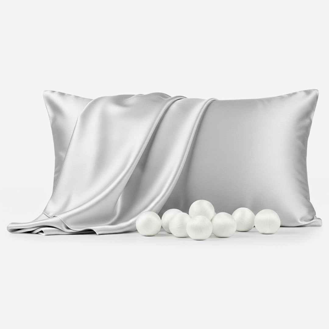 Silver grey silk sleep pillowcase with smooth sheen folded alongside white silk balls.