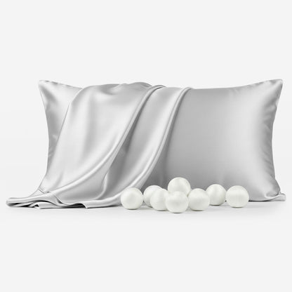 Silver grey silk sleep pillowcase with smooth sheen folded alongside white silk balls.