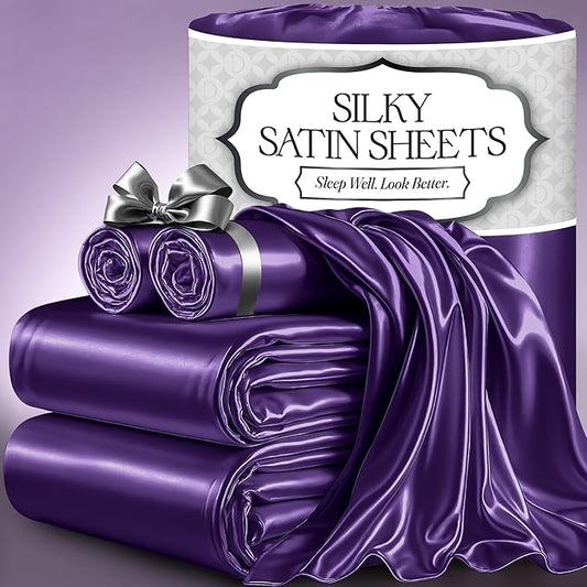 Purple satin sheet set with smooth, glossy finish, displayed folded and partially draped with silver ribbon accessory.