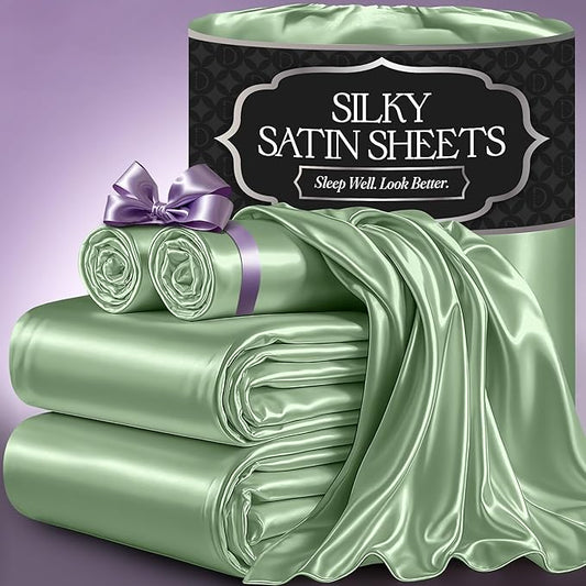 Sage green satin sheet set with smooth sheen, including folded sheets and a rolled pillowcase tied with lavender ribbon.